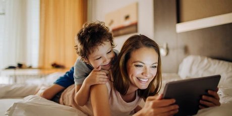 Family hotels in Berlin Mother and child lying on a bed and look at pictures on a tablet