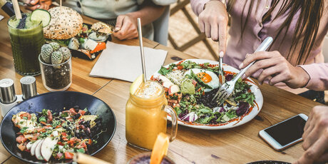 Hands view of young people eating brunch and drinking smoothies bowl with ecological straws in plastic free restaurant - Healthy lifestyle, food trends concept - Focus on top fork dish