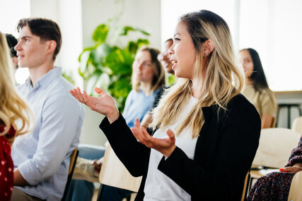 Young Woman Asking Question And Gesturing With Her Hands During Presentation