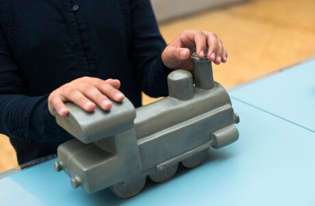 Hände ertasten das Modell einer Lokomotive