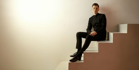 Richard Gowers sitzt im Anzug auf einer Treppe