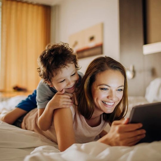 Family hotels in Berlin Mother and child lying on a bed and look at pictures on a tablet