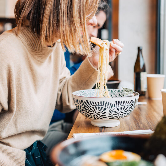 A young woman eats ramen soup at a counter in Berlin