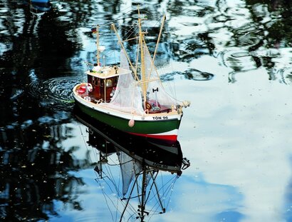 Ein grünes Modellschiff schwimmt auf dem Teich.