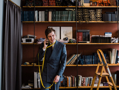 Maximilian Mogg am Telefon, mit einem mit einem Maßband um den Hals, in seinem Laden in Berlin