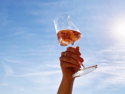 Eine Hand streckt ein Glas mit Roséwein in die Luft