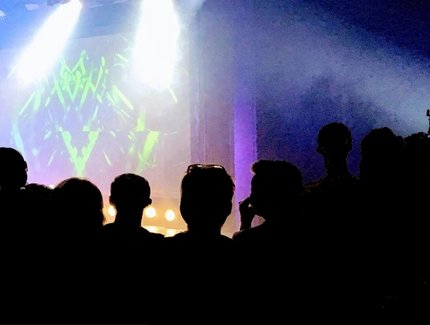 GRAFIK Menschen vor einer beleuchteten Bühne GRAFIK Menschen vor einer beleuchteten Bühne