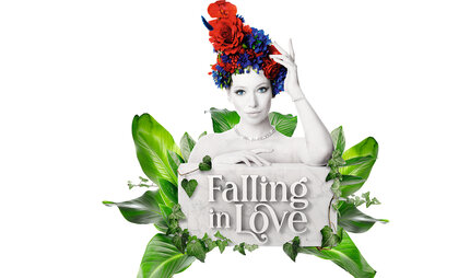 Eine Frau in Graustufen mit geblümtem Kopfschmuck posiert hinter einem Schild mit der Aufschrift "Falling in Love", umgeben von grünen Blättern.