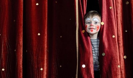 Boy dressed as a clown Child made up as a clown, behind a red curtain