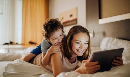 Family hotels in Berlin Mother and child lying on a bed and look at pictures on a tablet
